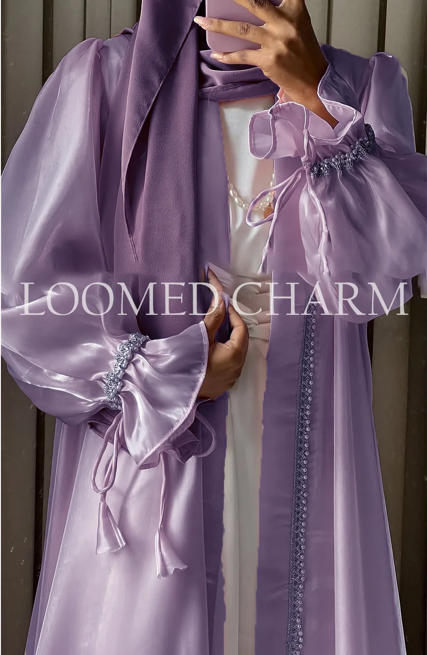 Luxurious Noya Silk Organza Shrug Abaya in soft pink with intricate crystal embellishments, featuring a satin inner, adjustable belt, and matching white chiffon scarf.